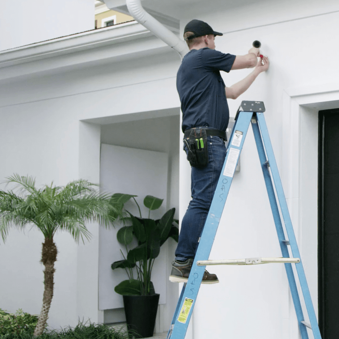 a man installs an exterior camera to a house. For the neighbourhood referral deal.