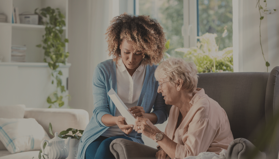 an in-home nurse helps an elderly patient hold a book to read